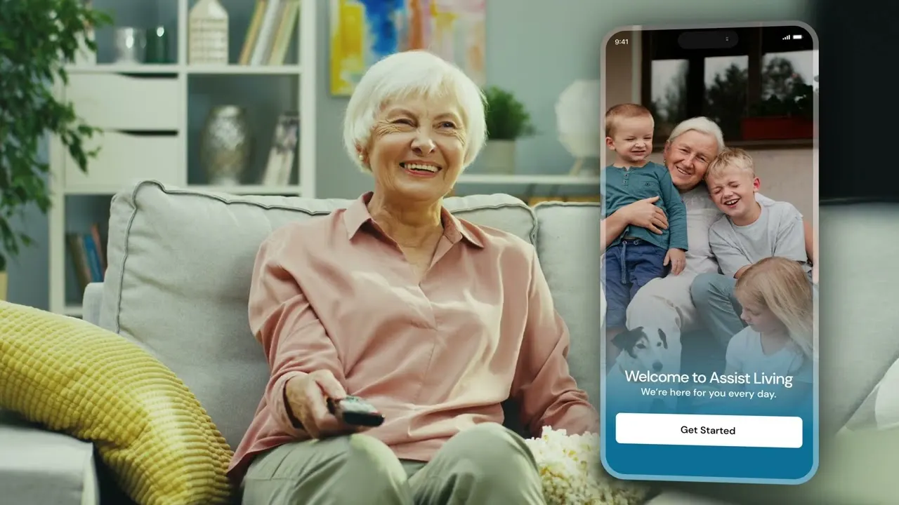 Standbild aus dem Promo-Video: Eine Seniorin sitzt lächelnd auf dem Sofa, daneben die Familien-App von Assist Living.